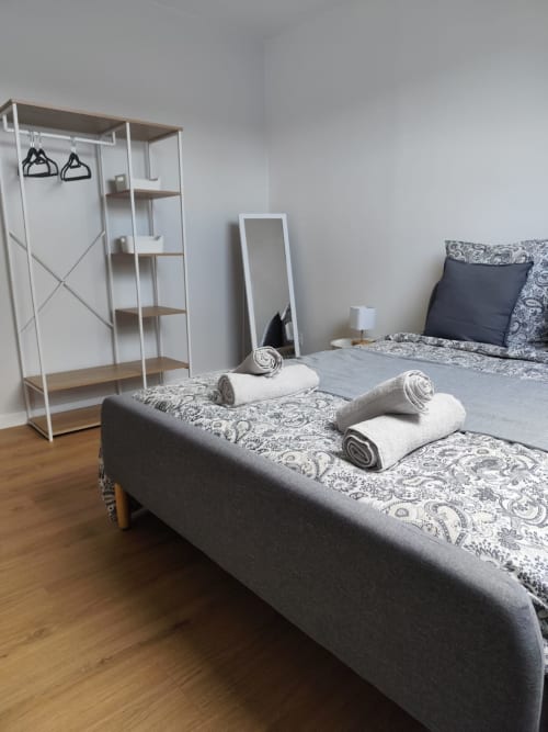 Chambre moderne à l'hôtel Accolade à Châteaudun avec lit gris, serviettes enroulées, armoire blanche et parquet