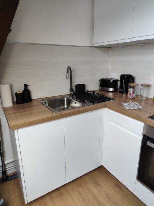 Cuisine moderne de l'appartement L'escale de La Loupe à l'hôtel Accolade, Châteaudun, avec placards blancs et plan de travail en bois