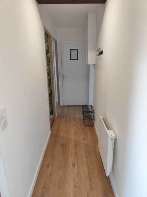 Étroit couloir de l'appartement Accolade à Châteaudun, avec parquet, murs blancs et radiateur