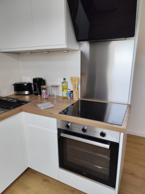 Cuisine moderne de l'appartement L'escale de La Loupe à l'hôtel Accolade, Châteaudun, avec armoires blanches et plan de travail en bois
