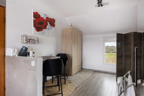 Chambre moderne du Petit Villeneuve avec fauteuils noirs, armoire en bois, tableau de coquelicots rouges et vue sur le jardin