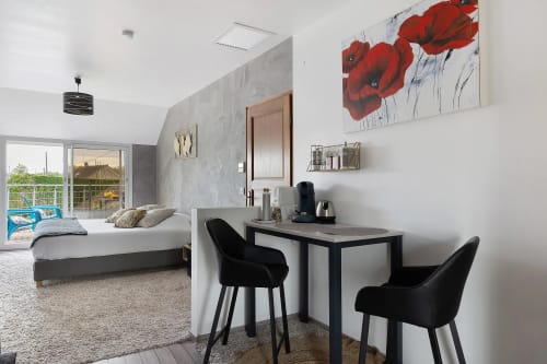 Chambre moderne au Petit Villeneuve avec bureau, chaises noires, tableau de coquelicots rouges et accès balcon vue jardin