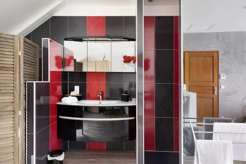 Salle de bain moderne du gîte Le Petit Villeneuve avec carrelage rouge et noir, vasque courbe, armoire miroir et chauffage