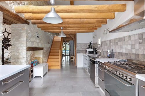 Cuisine moderne du gîte Le Pressoir avec poutres apparentes, électroménagers inox et murs en pierre