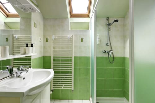 Salle de bain moderne avec carrelage vert et blanc, vasque, sèche-serviettes chauffant et douche vitrée au Petit Villeneuve