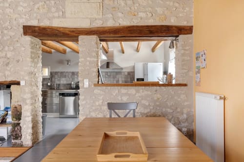 Cuisine ouverte et salle à manger du gîte Le Pressoir avec murs en pierre brute, poutres en bois et table à manger en bois