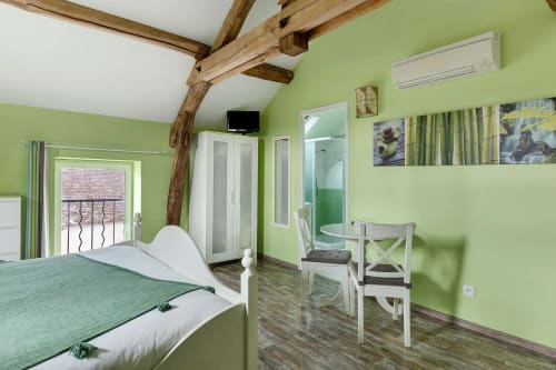 Chambre verte éclatante avec poutres apparentes, lit blanc, salle de bain attenante, table 