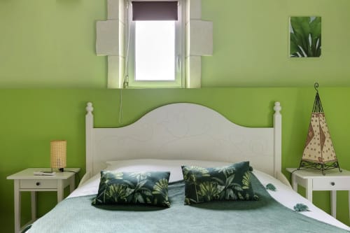 Chambre verte éclatante avec lit blanc, coussins tropicaux, tables de nuit et fenêtre au Petit Villeneuve, Saint-Georges-sur-Cher
