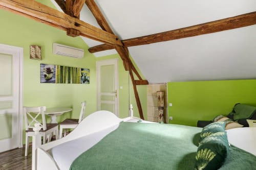 Chambre verte éclatante avec poutres en bois apparentes, mobilier blanc et literie verte au gîte Le Petit Villeneuve