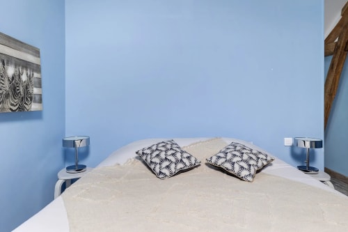 Chambre moderne aux murs bleus, lit blanc, oreillers motifs et lampes de chevet à Le Petit Villeneuve gîte le pressoir