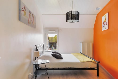Chambre moderne avec mur d'accent orange, lit en métal noir et vue sur le jardin au Petit Villeneuve, Saint-Georges-sur-Cher