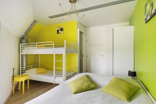 Chambre aux couleurs vives jaune et vert citron, avec lits superposés blancs et lit simple garni de coussins verts au Petit Villeneuve
