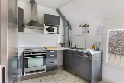Cuisine moderne du gîte Le Petit Villeneuve avec électroménagers inox, placards foncés, carrelage blanc et vue sur le jardin