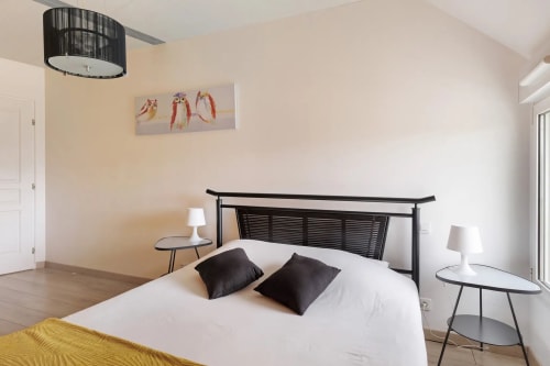 Chambre moderne au Petit Villeneuve avec lit queen, tête de lit noire, draps blancs, lampes de chevet et œuvres d'art