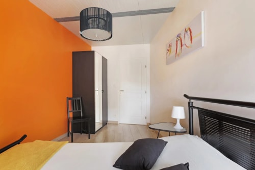Chambre moderne au Petit Villeneuve avec un mur d'accent orange audacieux, lit à cadre noir, lampe blanche et décoration contemporaine