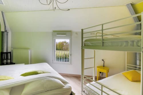Chambre lumineuse avec lits superposés, lit simple aux oreillers verts, table de nuit jaune, vue sur le jardin au Petit Villeneuve