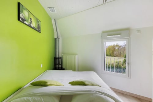 Chambre lumineuse avec mur d'accent vert citron, lit blanc et coussins verts, vue sur le jardin depuis la porte du Petit Villeneuve B&B