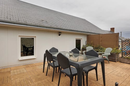Espace repas sur la terrasse du gîte Le Petit Villeneuve avec chaises en rotin noir, table en verre et vue sur le jardin