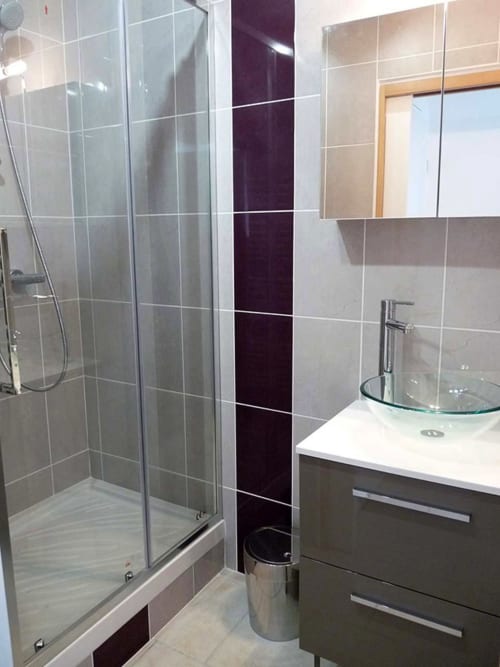 Salle de bain moderne au gîte Le Petit Villeneuve avec douche vitrée, vasque et carreaux foncés