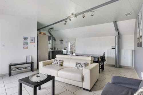 Spacieux séjour du gîte avec canapé crème, table basse noire et cuisine ouverte au Petit Villeneuve B&B