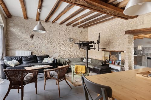 Intérieur rustique de chaumière en pierre avec poutres apparentes, canapé noir en cuir, chaises en osier, table de bois et murs de pierre
