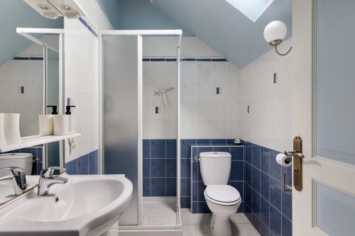 Salle de bains moderne du gîte Le Petit Villeneuve avec carrelage bleu marine et blanc, douche vitrée, double vasque et toilettes