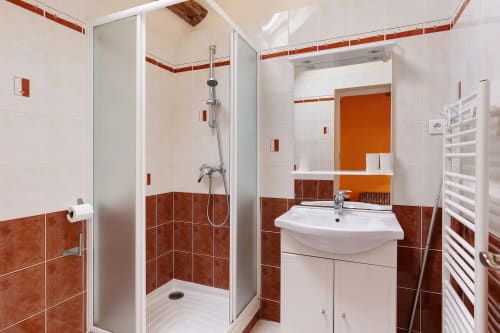 Salle de bains moderne avec carrelage rouille et blanc, douche vitrée, lavabo sur colonne blanc et porte-serviettes chauffant au Petit
