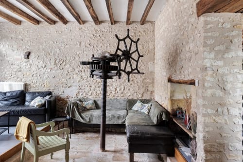 Intérieur rustique de chaumière en pierre avec poutres apparentes, canapés noirs, décor de roue de bateau, style traditionnel