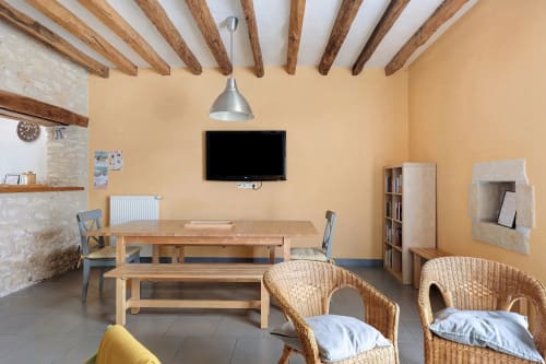 Séjour spacieux au Petit Villeneuve avec poutres en bois apparentes, table à manger, chaises en osier et téléviseur