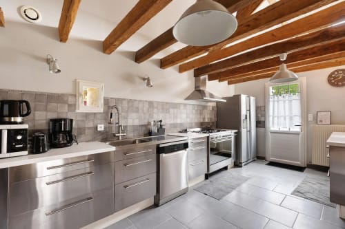 Cuisine moderne avec appareils en acier inoxydable, poutres en bois et carrelage au gîte Le Petit Villeneuve