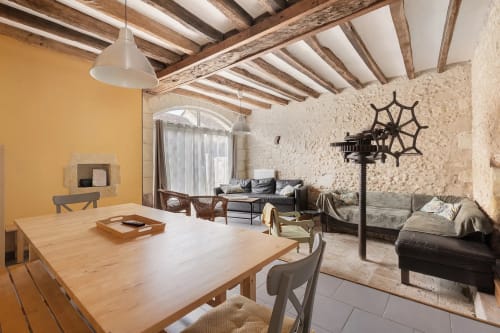 Intérieur rustique du Petit Villeneuve avec poutres en bois, table à manger, salon aux murs de pierre et jardin
