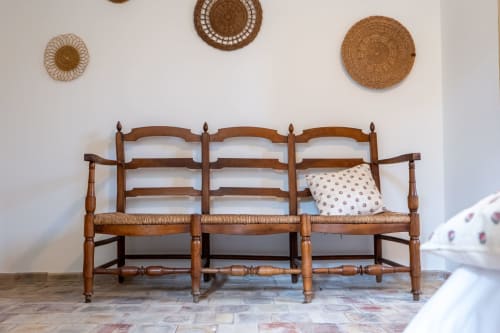 Rustic wooden bench with woven rush seat at Mas Bella Cortis B&B, La Garde-Adhémar, decorated with woven wall baskets