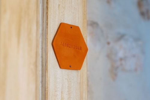 Orange hexagonal plaque mounted on wooden wall at Mas Bella Cortis bed and breakfast in La Garde-Adhémar, France
