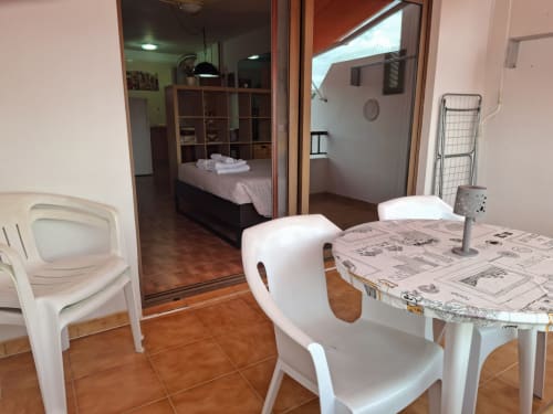Modern apartment dining area with white chairs, table with newspaper, open glass doors to bedroom, Costa Adeje, Tenerife