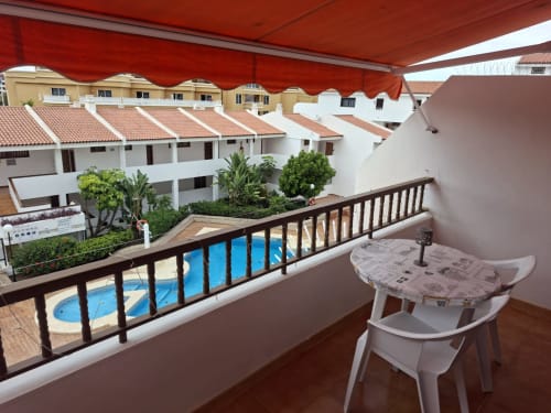Balcony with pool view at Marigold apartments in Costa Adeje, Tenerife. Red awning, white furniture, shared pool and tropical