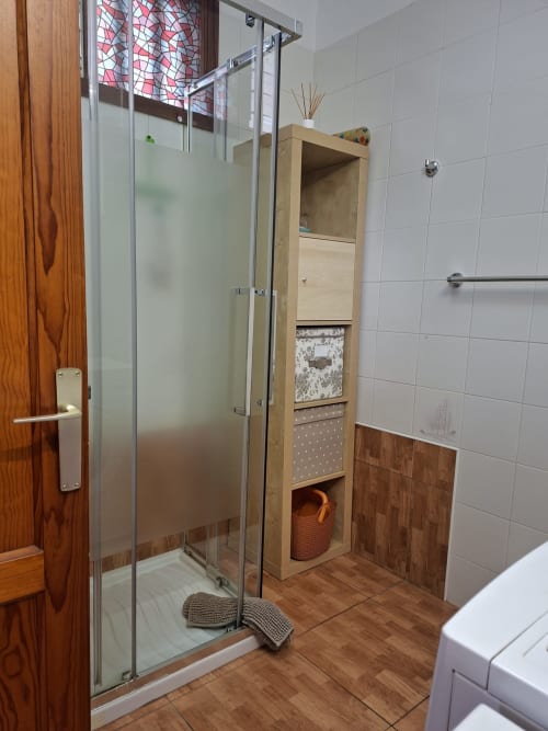Modern bathroom in Costa Adeje apartment with glass shower enclosure, wooden storage unit, and white tile walls