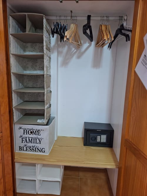 Organized closet with wooden hangers, shelving unit with 'Home Family Blessing' text, and safe in Costa Adeje apartment