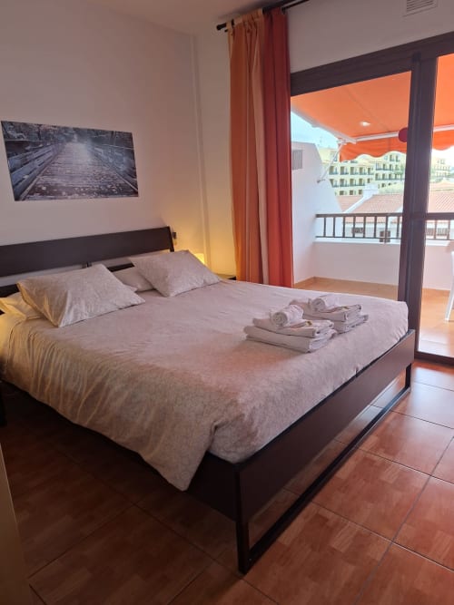 Modern bedroom in Costa Adeje apartment with queen bed, ocean view balcony, orange curtains, and folded towels