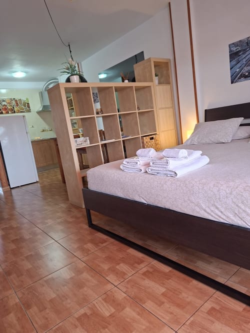 Modern bedroom at Marigold Property in Costa Adeje with bed, wooden shelving, kitchenette, and folded towels