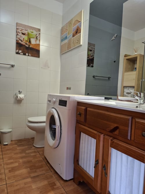 Modern bathroom with washing machine, wooden vanity, white tiles, and gray accent wall in Costa Adeje apartment