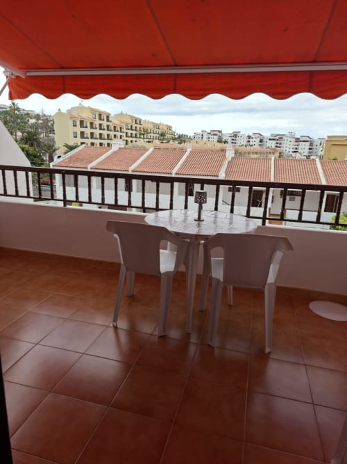 Spacious balcony with red awning overlooking Costa Adeje townscape, furnished with dining table and chairs