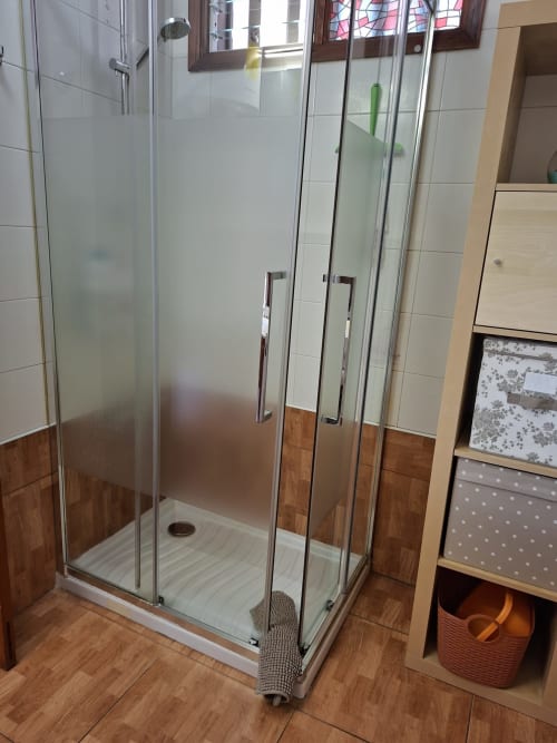 Modern glass shower enclosure in Costa Adeje apartment bathroom with tiled walls and wooden accents