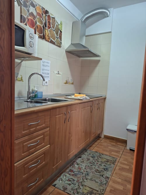 Modern kitchen with wooden cabinets, stainless steel sink, microwave, and cooker at Marigold apartment in Costa Adeje,