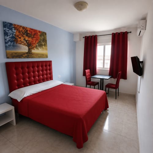 Moderno dormitorio doble en Hostal Europa de Aldaia con cama roja, paredes azules y zona de escritorio