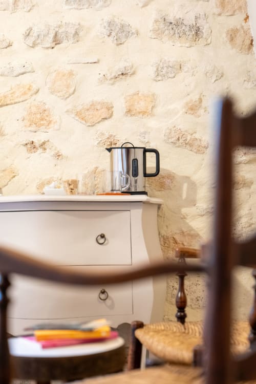 Bouilloire électrique moderne sur commode blanche devant mur en pierre rustique au Mas Bella Cortis, gîte à La Garde-Adhémar