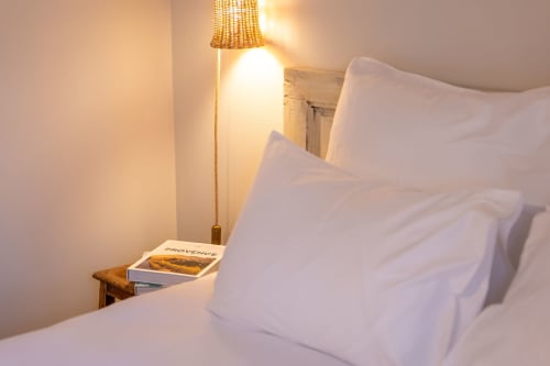 Chambre accueillante au Mas Bella Cortis avec oreillers blancs, lampe chaleureuse et livre de Provence sur la table de nuit