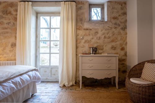 Charming bedroom at Mas Bella Cortis B&B in La Garde-Adhémar with floral wallpaper, cream curtains, and wicker chair