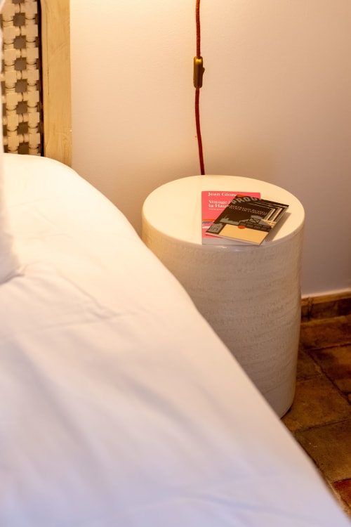 Cozy bedroom detail at Mas Bella Cortis showing white bedding, cylindrical nightstand with books, and warm lighting in La