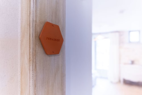 Hexagonal terracotta room tag reading 'PROVENCE' on wooden door frame at Mas Bella Cortis boutique hotel in La Garde-Adhémar