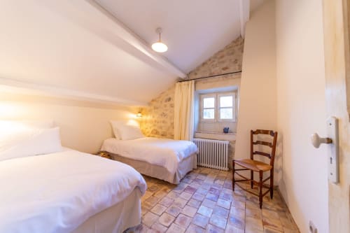Twin bedroom at Mas Bella Cortis B&B in La Garde-Adhémar with white beds, terracotta floor, and rustic stone accent wall